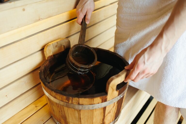 Close-up of a man in a sauna scooping water with a ladle from a wooden bucket