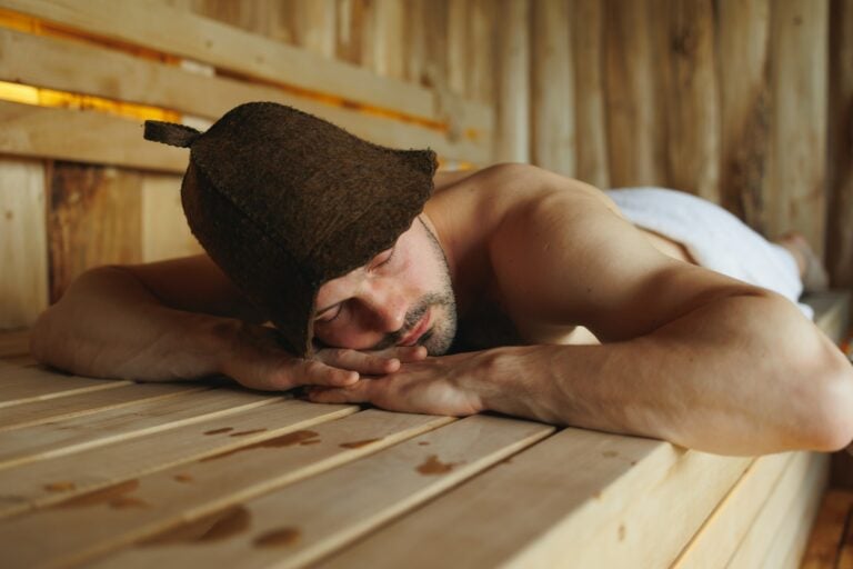 Mann in Saunakilt für Herren und mit Saunahut liegt entspannt in der Sauna